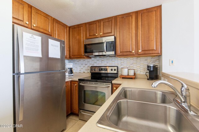 kitchen featuring sink, a textured ceiling, decorative backsplash, light tile patterned floors, and appliances with stainless steel finishes