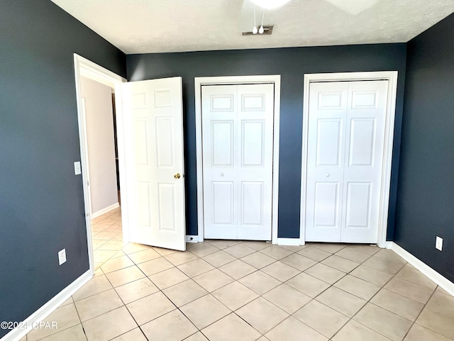 unfurnished bedroom featuring two closets, light tile patterned floors, and a textured ceiling