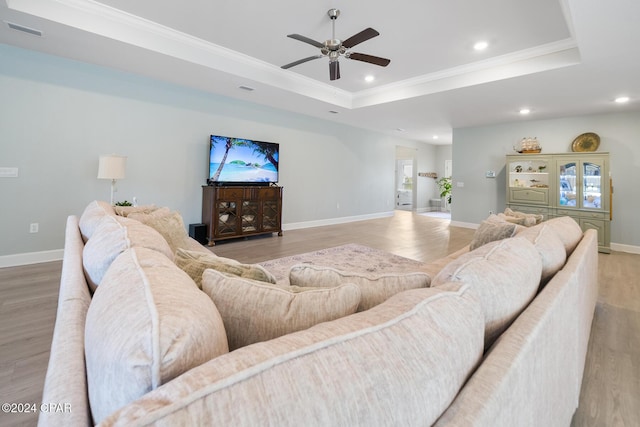 living room featuring ceiling fan, a raised ceiling, light wood-type flooring, and crown molding