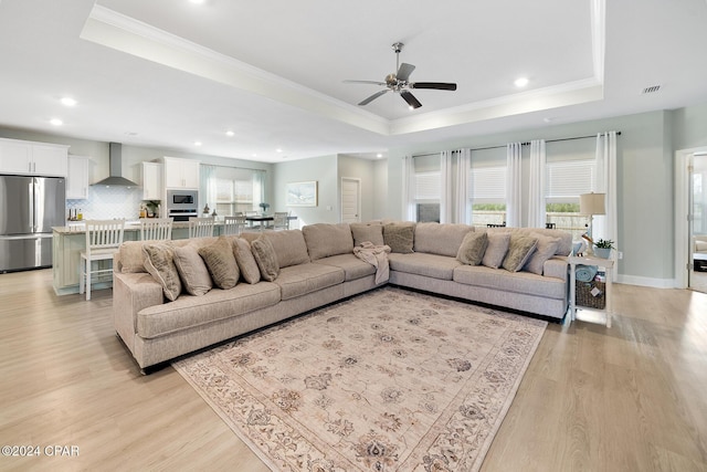 living room featuring a raised ceiling, ceiling fan, crown molding, and light wood-type flooring