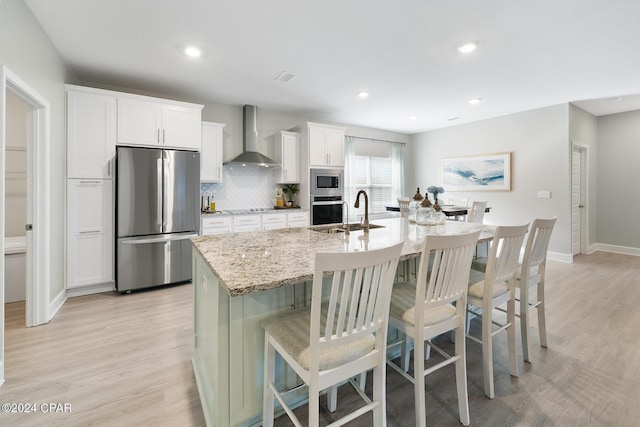 kitchen with white cabinets, sink, wall chimney exhaust hood, an island with sink, and stainless steel appliances