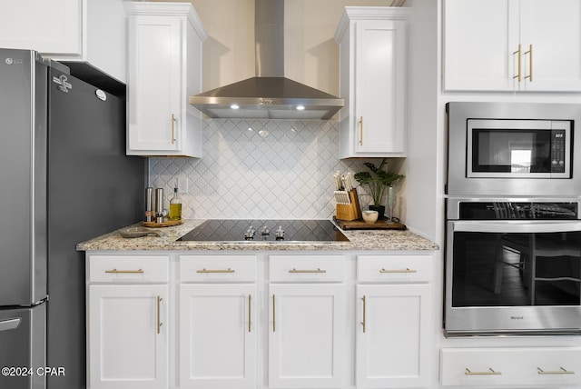 kitchen featuring tasteful backsplash, white cabinets, wall chimney range hood, and appliances with stainless steel finishes