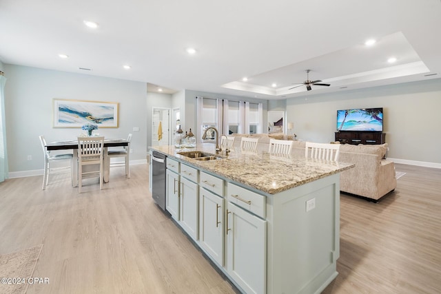 kitchen with dishwasher, a raised ceiling, sink, light stone countertops, and an island with sink