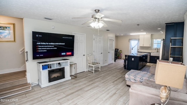 living room featuring a textured ceiling, light wood-type flooring, ceiling fan, and sink