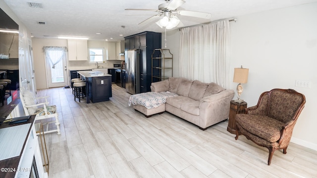 living room featuring a textured ceiling, ceiling fan, sink, and light hardwood / wood-style flooring