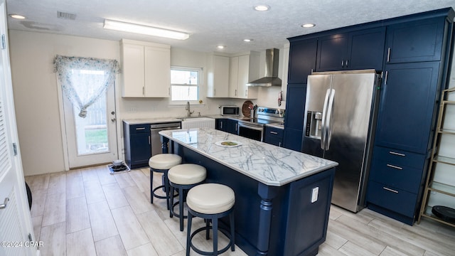 kitchen with appliances with stainless steel finishes, wall chimney exhaust hood, sink, white cabinets, and a center island