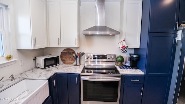 kitchen with white cabinets, stainless steel electric range oven, blue cabinetry, and wall chimney range hood