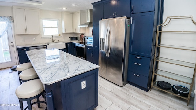 kitchen with appliances with stainless steel finishes, sink, wall chimney range hood, white cabinets, and a center island