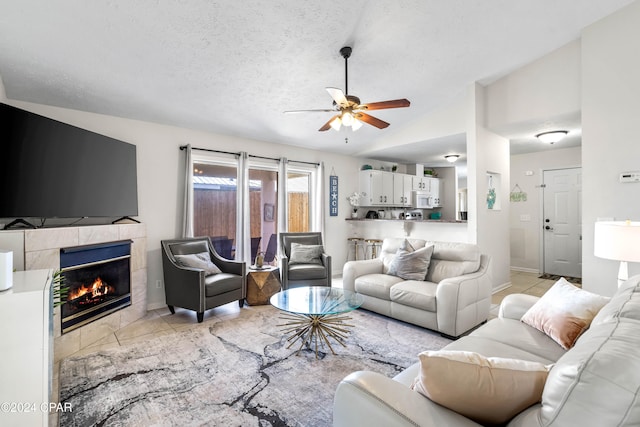 tiled living room featuring a textured ceiling, ceiling fan, lofted ceiling, and a tiled fireplace