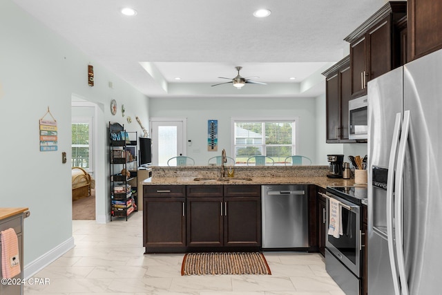 kitchen featuring kitchen peninsula, stainless steel appliances, ceiling fan, sink, and dark stone countertops