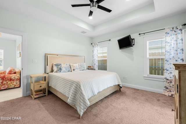 carpeted bedroom featuring a raised ceiling, multiple windows, and ceiling fan