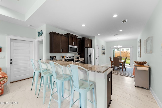 kitchen featuring a notable chandelier, a kitchen bar, light stone countertops, and appliances with stainless steel finishes