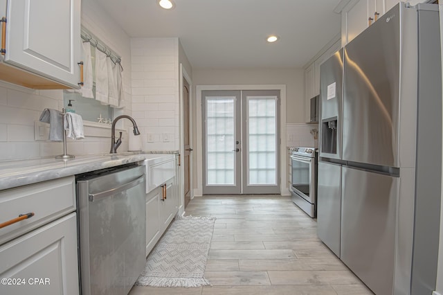 kitchen with french doors, backsplash, appliances with stainless steel finishes, white cabinetry, and light wood-type flooring