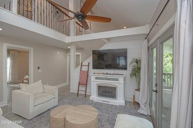 living room featuring a fireplace, a high ceiling, ceiling fan, wood finished floors, and baseboards