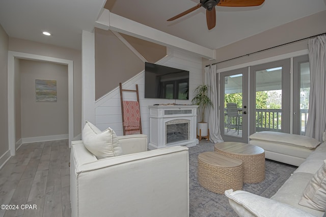 living area featuring a fireplace with raised hearth, ceiling fan, light wood-style flooring, recessed lighting, and french doors