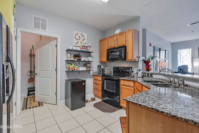 kitchen with dark stone counters, sink, light tile patterned floors, and black appliances