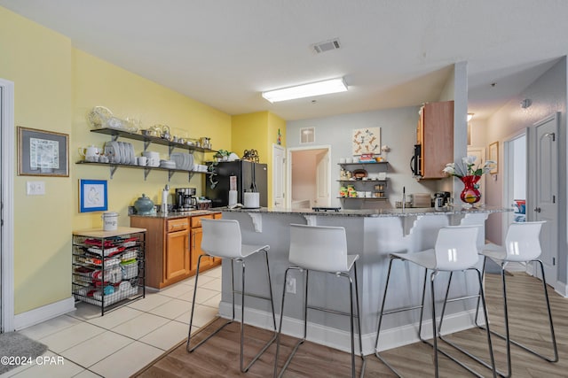 kitchen featuring a kitchen breakfast bar, black refrigerator, light stone countertops, light hardwood / wood-style floors, and kitchen peninsula