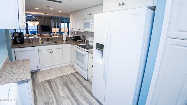 kitchen with white appliances, dark stone counters, sink, light wood-type flooring, and white cabinetry