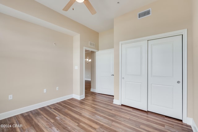 unfurnished bedroom with ceiling fan with notable chandelier, light hardwood / wood-style flooring, and a closet