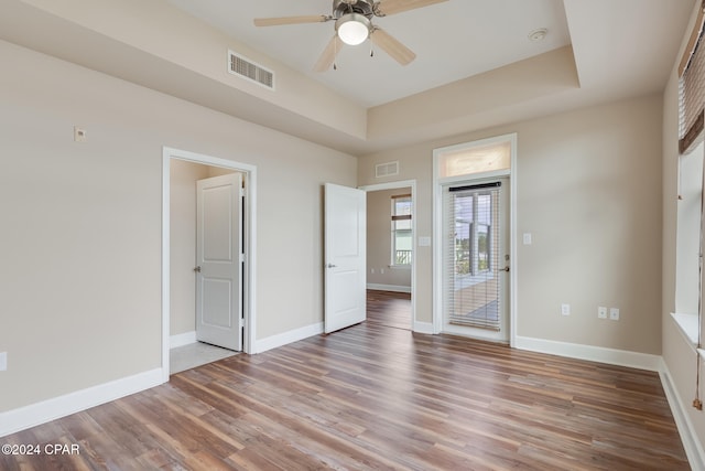 empty room featuring a raised ceiling, ceiling fan, and light hardwood / wood-style flooring