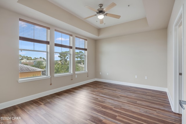 empty room with ceiling fan, dark hardwood / wood-style flooring, and a tray ceiling