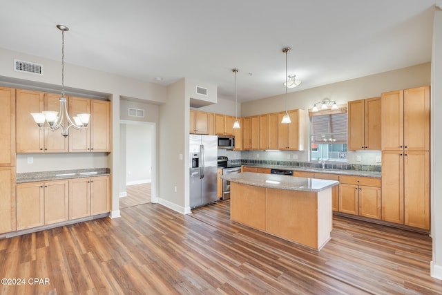 kitchen featuring a center island, hanging light fixtures, light stone counters, wood-type flooring, and stainless steel appliances