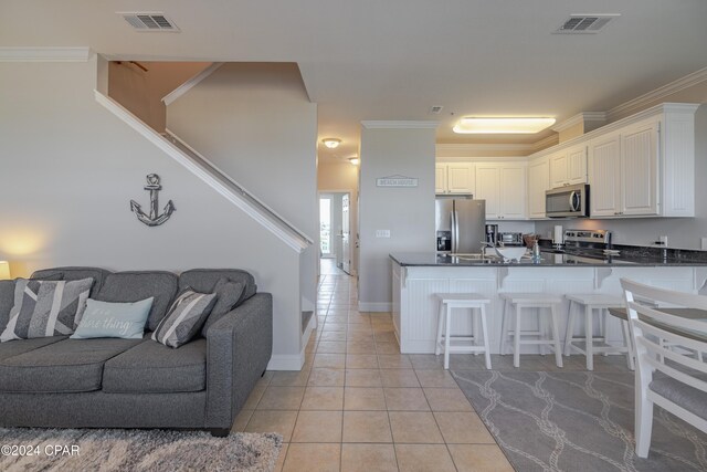 kitchen with kitchen peninsula, appliances with stainless steel finishes, crown molding, light tile patterned floors, and white cabinets