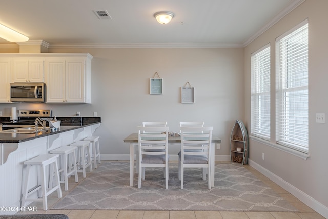 kitchen featuring stainless steel appliances, white cabinets, dark stone counters, light tile patterned flooring, and ornamental molding