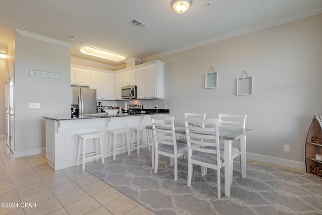 kitchen with stainless steel appliances, light tile patterned floors, kitchen peninsula, white cabinets, and ornamental molding