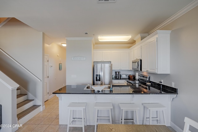 kitchen featuring kitchen peninsula, appliances with stainless steel finishes, a kitchen bar, crown molding, and white cabinets