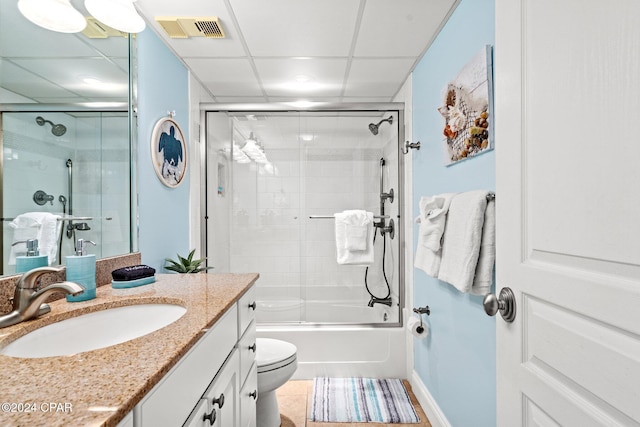 full bathroom featuring combined bath / shower with glass door, vanity, toilet, and a drop ceiling