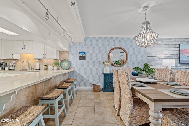 dining space with sink, rail lighting, an inviting chandelier, crown molding, and light tile patterned floors