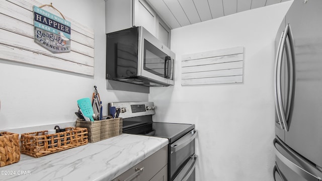 kitchen with gray cabinetry, light stone counters, and appliances with stainless steel finishes