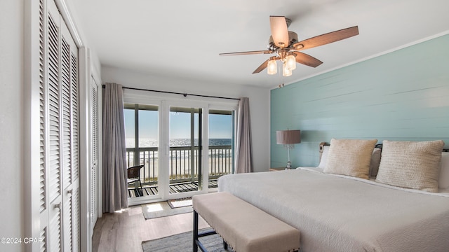 bedroom with access to exterior, ceiling fan, wood walls, hardwood / wood-style floors, and a water view