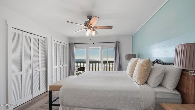 bedroom with access to outside, a water view, ceiling fan, wood-type flooring, and multiple closets