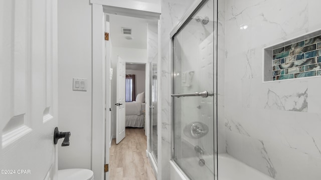 bathroom with hardwood / wood-style flooring, toilet, and enclosed tub / shower combo