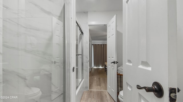 bathroom with hardwood / wood-style flooring, toilet, and bath / shower combo with glass door