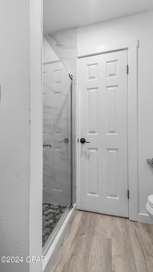 bathroom featuring toilet, a shower with shower door, and hardwood / wood-style flooring