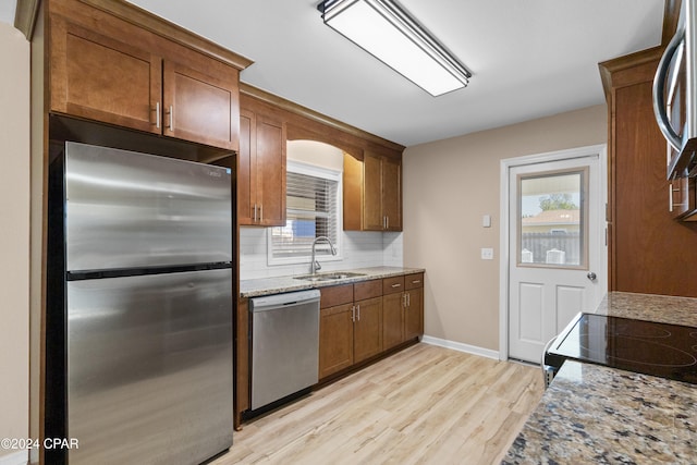 kitchen with backsplash, sink, light stone countertops, light wood-type flooring, and appliances with stainless steel finishes