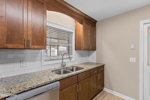 kitchen featuring light stone countertops, tasteful backsplash, stainless steel dishwasher, sink, and light hardwood / wood-style floors