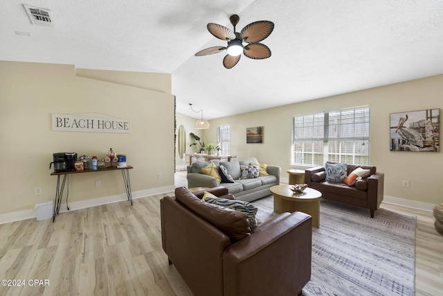 living room with ceiling fan, lofted ceiling, a textured ceiling, and light hardwood / wood-style floors