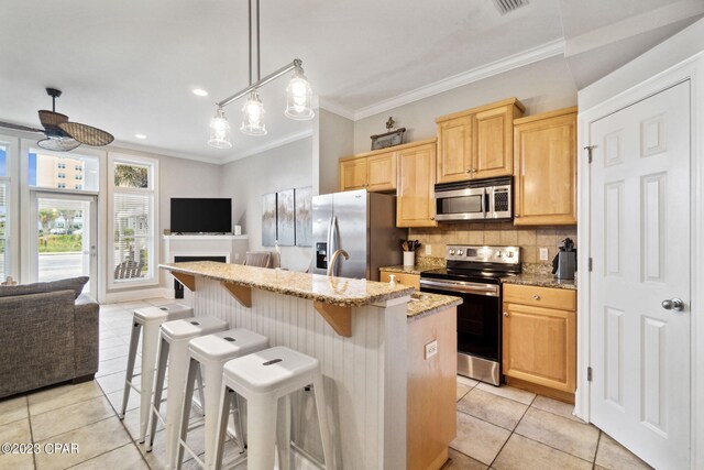 kitchen featuring pendant lighting, light stone counters, stainless steel appliances, and an island with sink