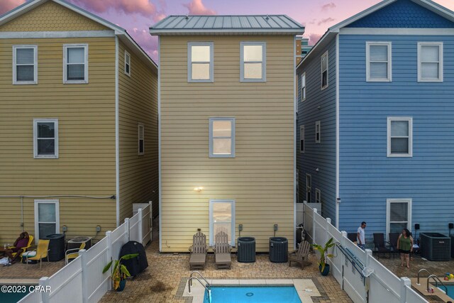 back house at dusk with a fenced in pool and central air condition unit