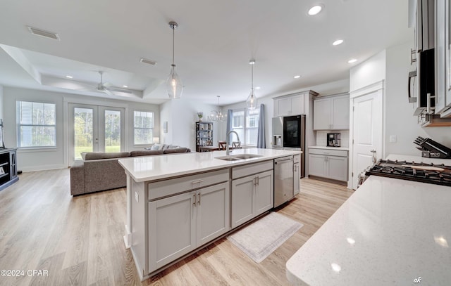 kitchen with a kitchen island with sink, a raised ceiling, hanging light fixtures, sink, and light hardwood / wood-style floors