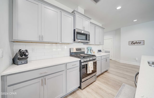 kitchen with gray cabinets, light wood-type flooring, tasteful backsplash, light stone counters, and stainless steel appliances