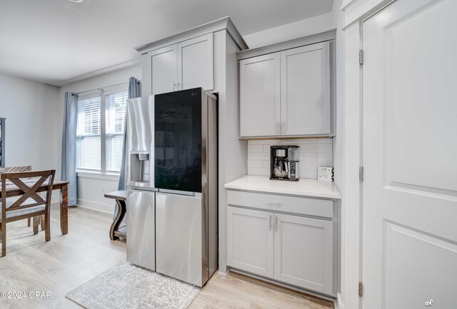 kitchen featuring decorative backsplash, stainless steel refrigerator with ice dispenser, light wood-type flooring, and gray cabinets