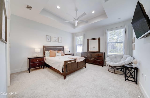 carpeted bedroom featuring ceiling fan, a tray ceiling, and multiple windows