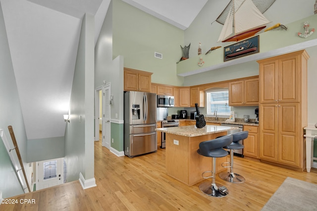 kitchen with stainless steel appliances, a kitchen breakfast bar, light hardwood / wood-style flooring, high vaulted ceiling, and a kitchen island