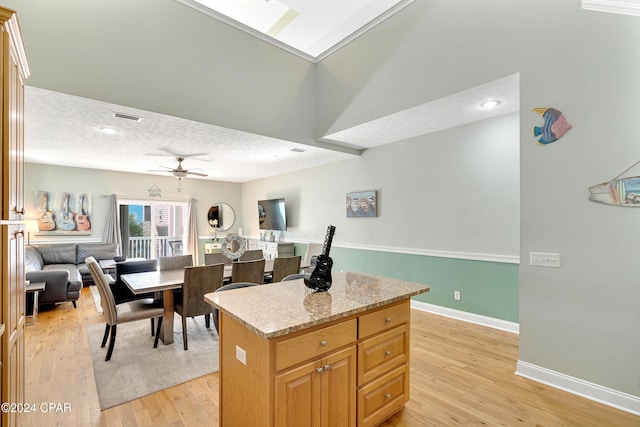 kitchen featuring a center island, ceiling fan, light wood-type flooring, a textured ceiling, and light stone counters