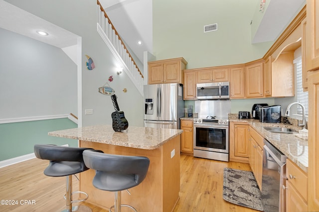 kitchen with sink, light brown cabinets, light stone counters, appliances with stainless steel finishes, and light wood-type flooring